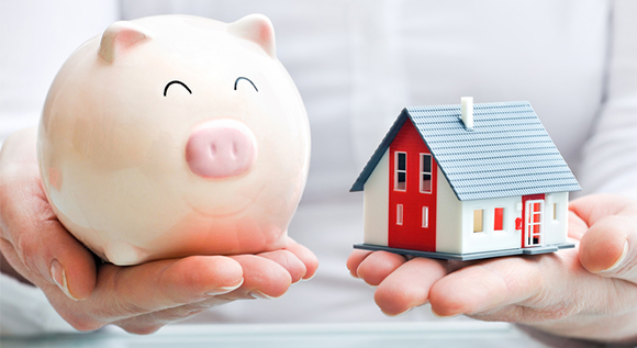 Person holding piggy bank and model house on each hand.