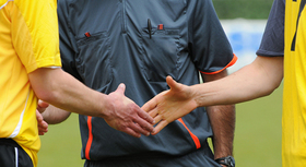 Two soccer players shaking hands in front of a referee.