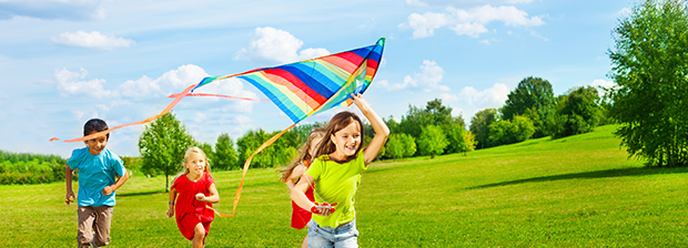 Kids running across a meadow playing with a kite.