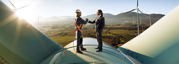 Two men shaking hands on top of a wind generator