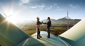 Two men shaking hands on top of a wind generator