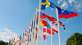 Fahnen der EU-Mitgliedsstaaten wehen im Wind, blauer Himmel im Hintergrund