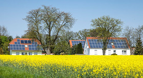 Mehrfamilienhäuser mit Fotovoltaikanlagen auf dem Dach und Rapsfeld im Vordergrund