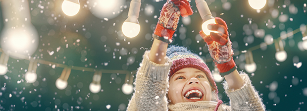 Lachendes Kind im Schnee schraubt Glühbirne in Lichterkette fest
